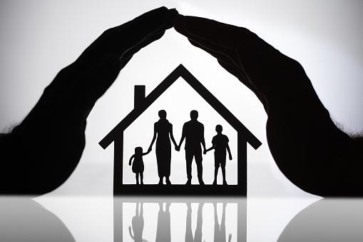 Hands covering small figures of a family inside a home